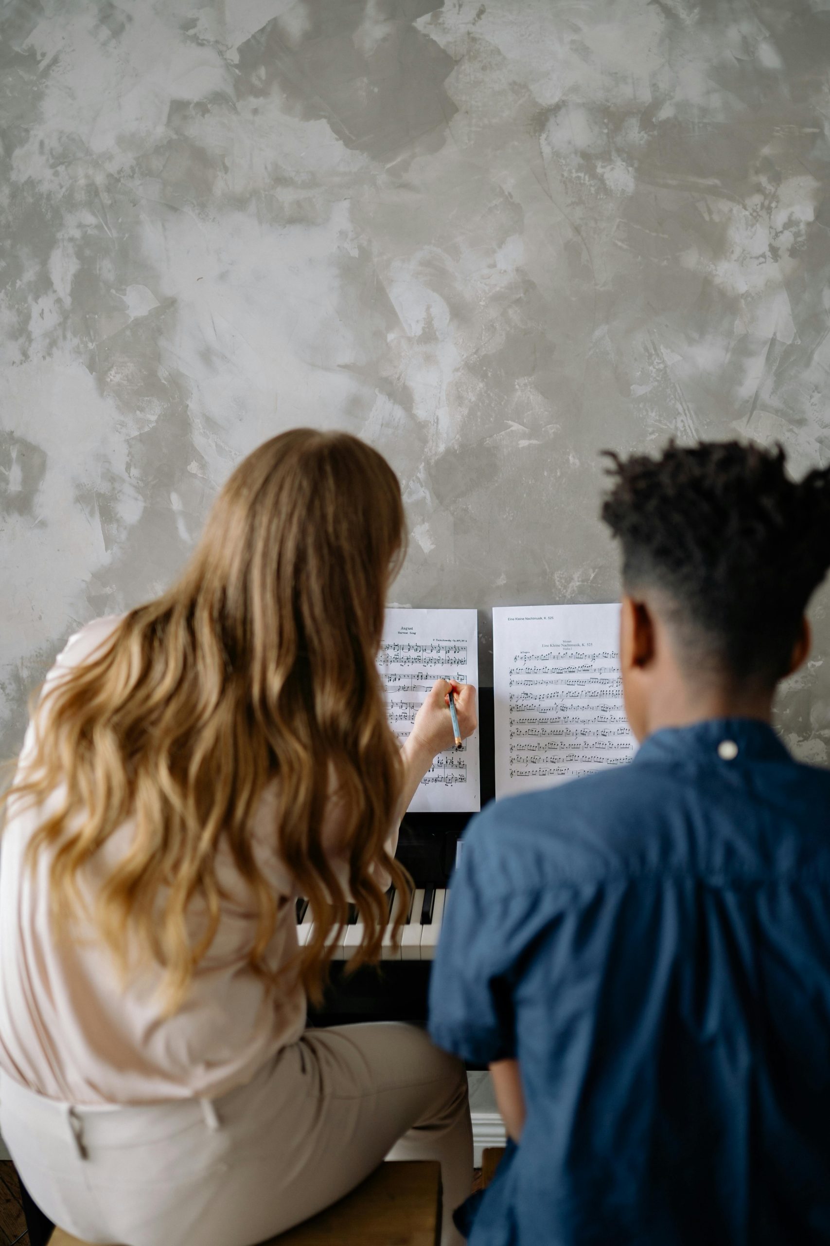 Back view of a woman teaching a child piano, focusing on musical notes.